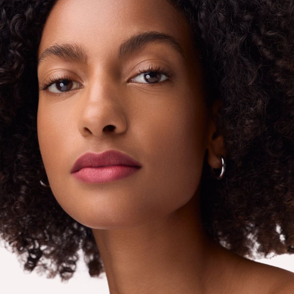 Portrait d'une femme portant du rouge à lèvres rose. Elle porte des créoles argentées.