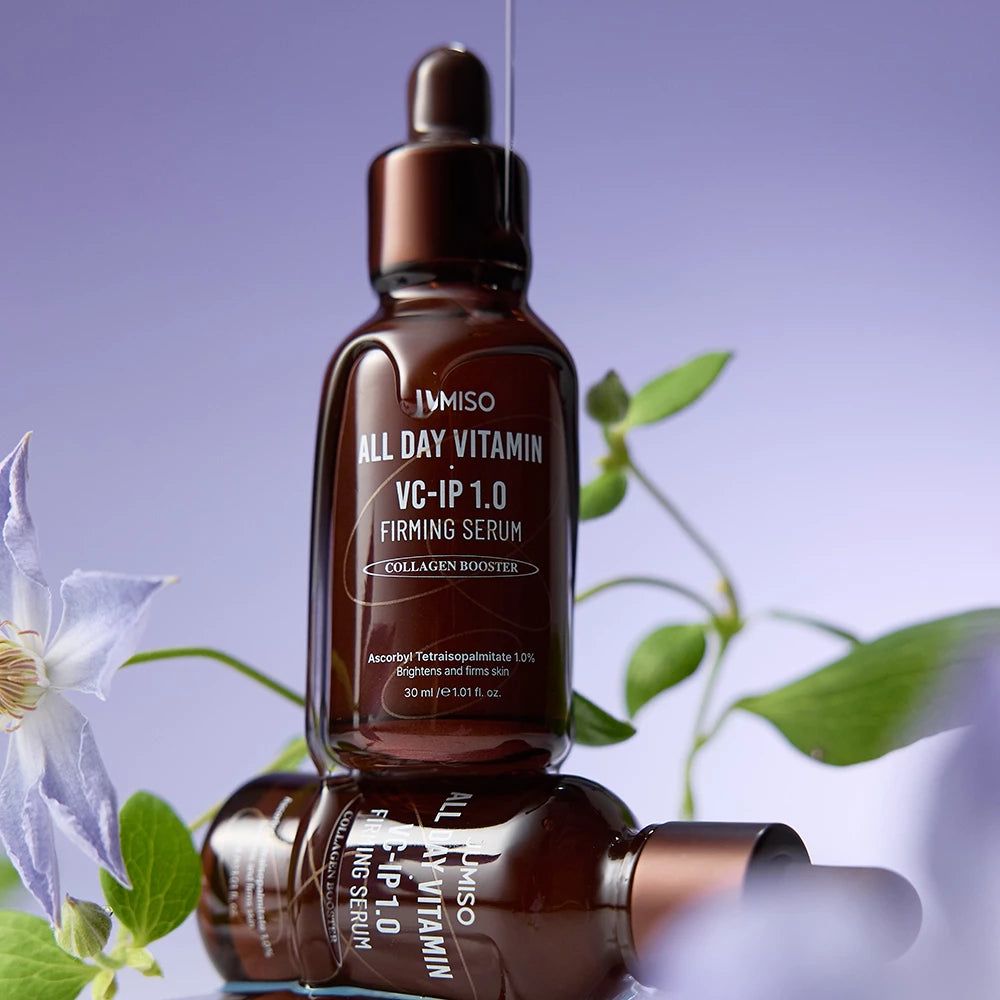 Twee JUMISO All Day Vitamin VC-IP 1.0 Firming Serum flessen gestapeld met bloemen.