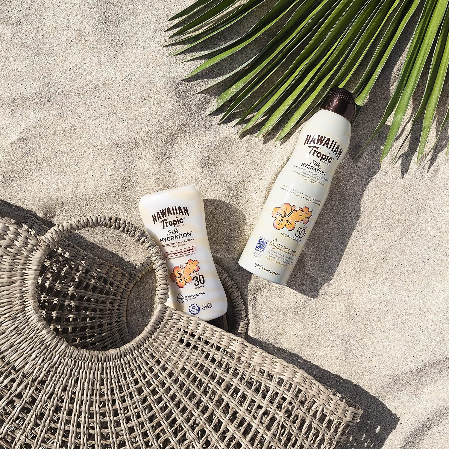 Deux flacons de lotion solaire sur le sable. Un Hawaiian Tropic Silk Hydration, SPF 30, l'autre SPF 50.