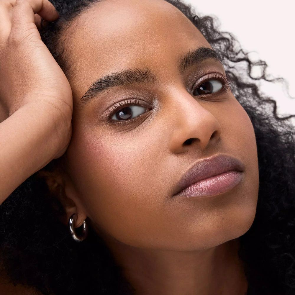 Gros plan d'une femme maquillée. Elle porte un fard à paupières rose et du rouge à lèvres. Ses cheveux sont bouclés et foncés.