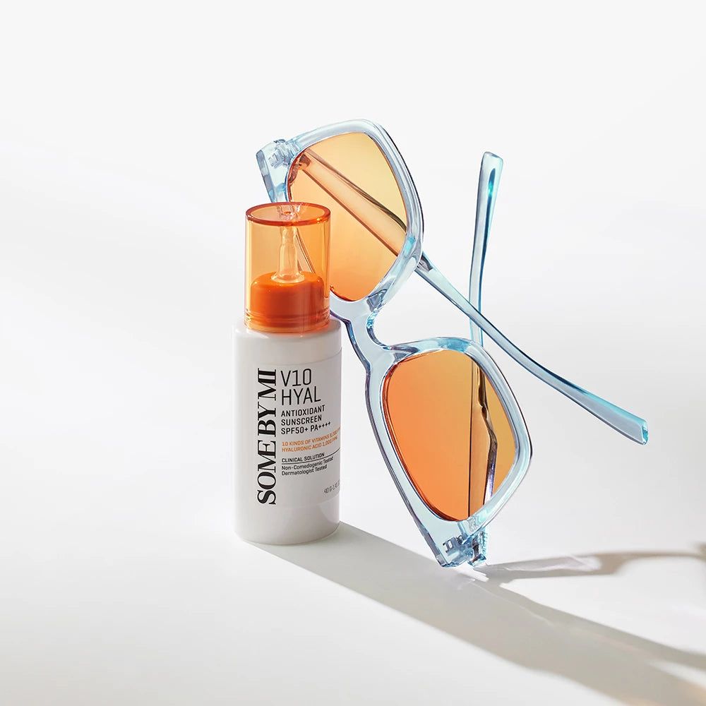 Flacon blanc avec bouchon orange et lunettes de soleil. Inscription : V10 Hyal Antioxidant Sunscreen SPF 50+ PA++++.
