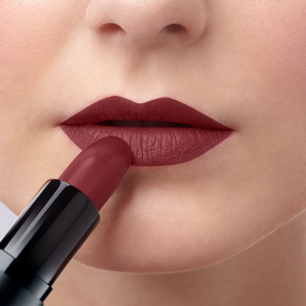 Lipstick wordt op lippen aangebracht. Rode lipstick in zwarte huls. Close-up.