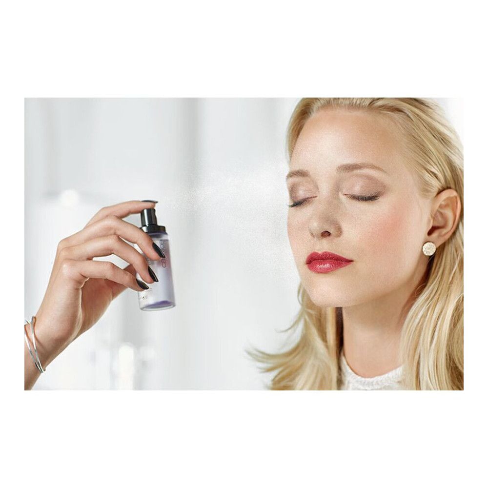 Een hand spuit een spray op het gezicht van een vrouw. De spray is Catrice Prime and Fine.