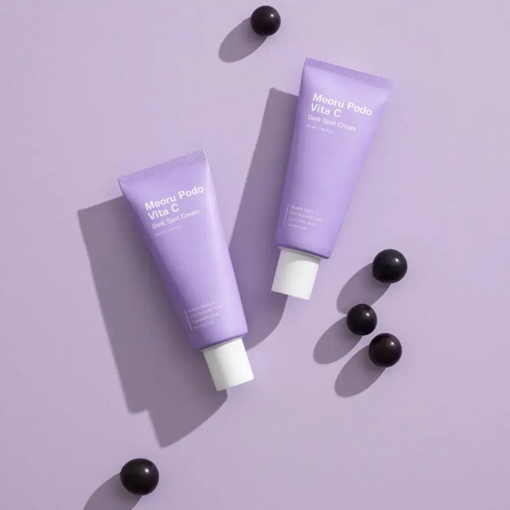 Deux tubes violets, à côté de baies foncées. Inscription : Meoru Podo Vita C Dark Spot Cream.