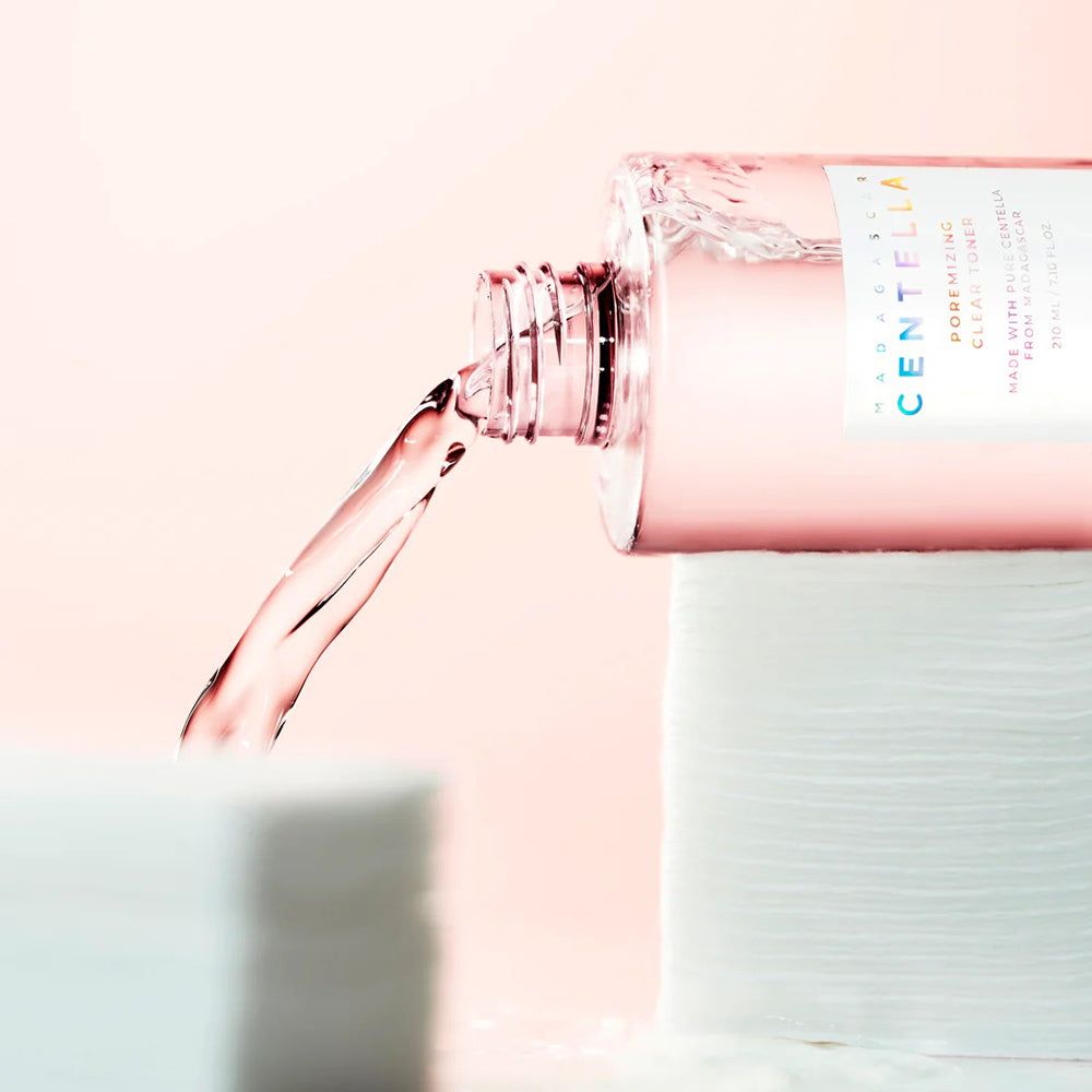 Fles giet vloeistof op wattenschijfjes. Fles met tekst: CENTELLA, POREMIZING CLEAR TONER, SKIN1004. Roze vloeistof.