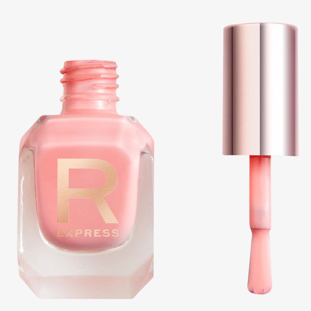 Een lichtroze nagellak in een zeshoekig glazen flesje met een goudkleurig 'R'-logo. De kwast is eruit gehaald en toont de kleur.