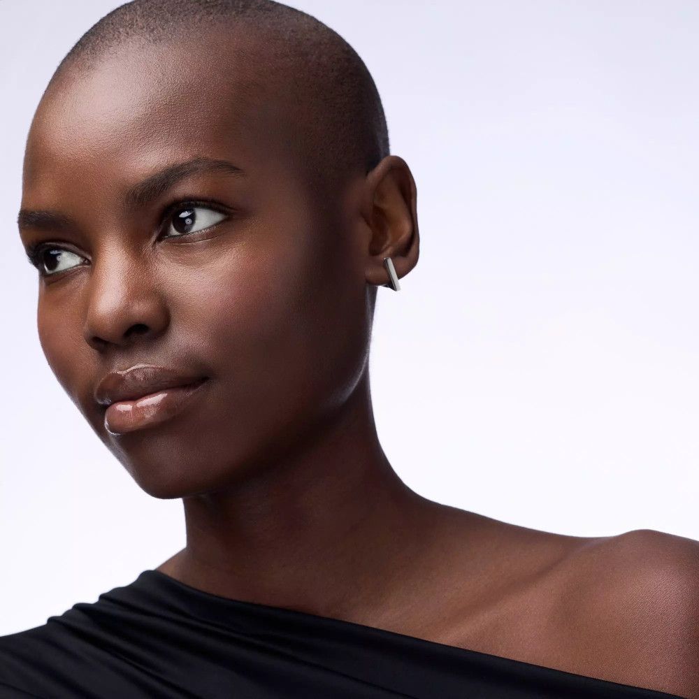 Portrait d'une femme à la peau foncée et aux cheveux rasés. Elle porte un haut noir et des boucles d'oreilles.