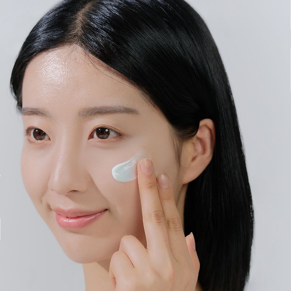 Vrouw brengt crème aan. Crème is lichtgroen. Gezicht en handen zichtbaar.