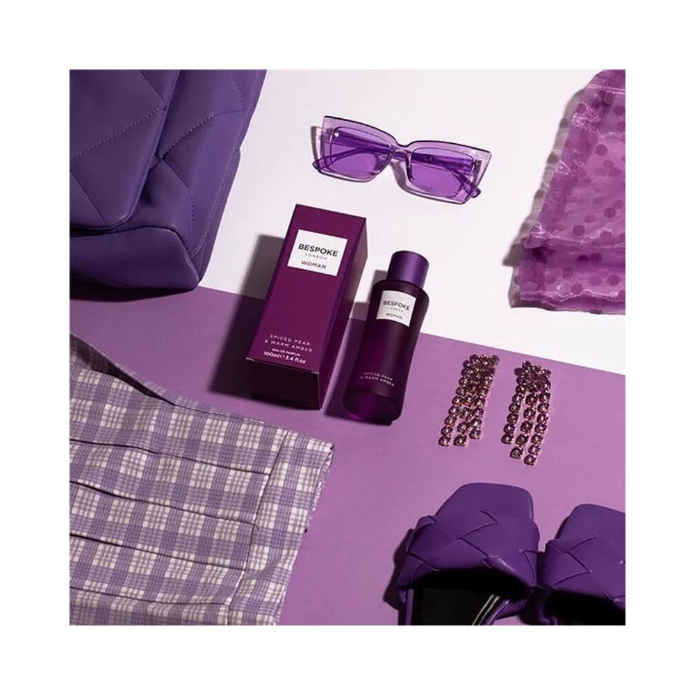 Flacon et boîte violets. Inscription: Bespoke London, Woman, Spiced Pear & Warm Amber. Entouré d'accessoires.