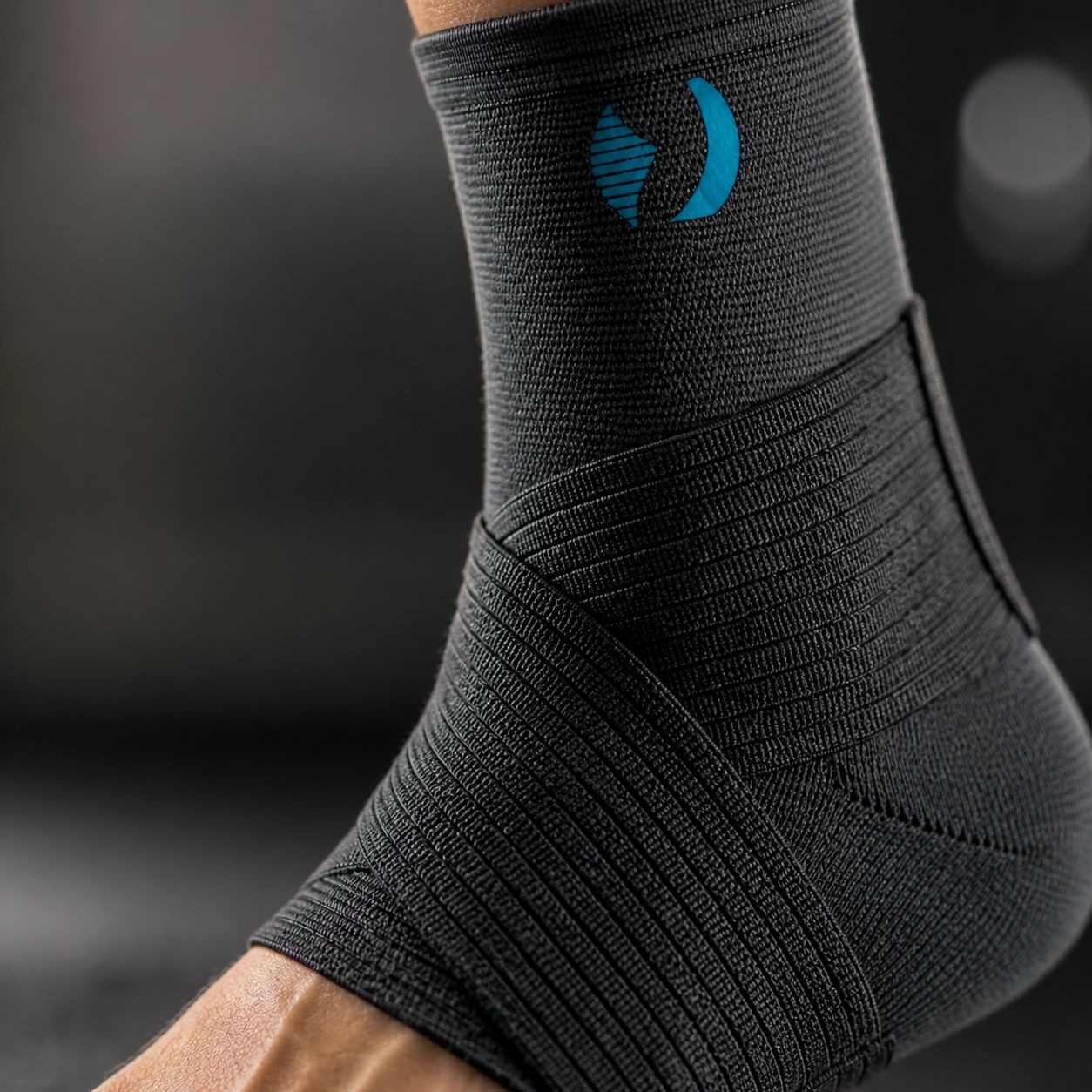 Close-up van een zwarte enkelbrace met blauw logo. Geweven materiaal met bandages.