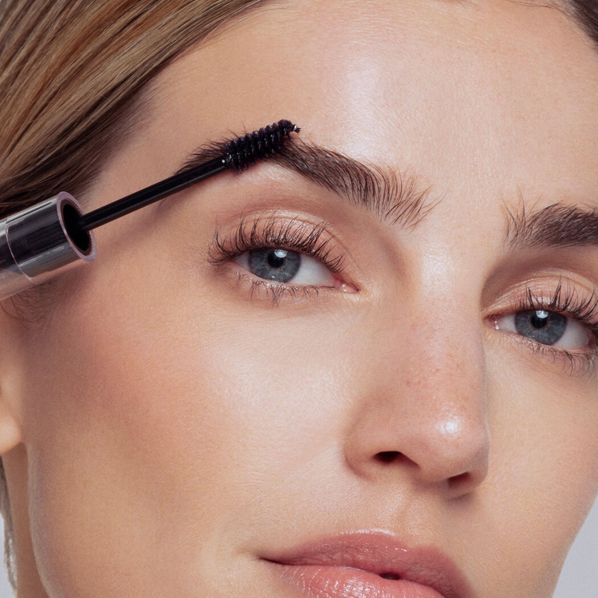 Femme appliquant du gel sourcils brun foncé avec un applicateur brosse.