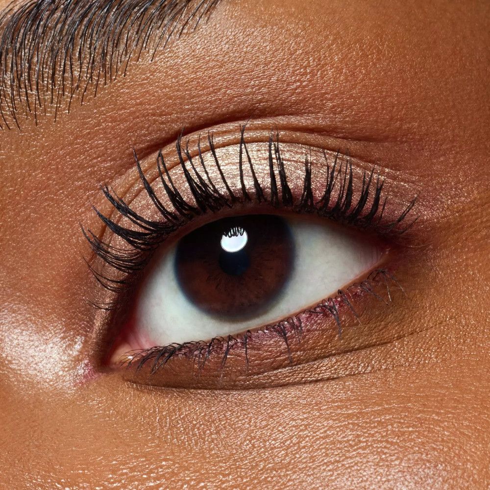 Gros plan sur un œil avec fard à paupières métallique. Longs cils. Peau foncée.