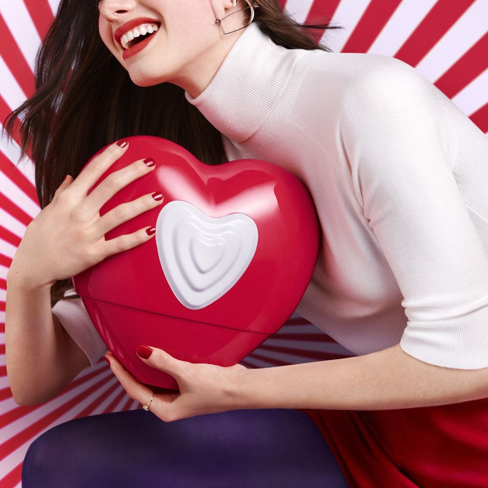 Femme tenant un flacon de parfum rouge en forme de cœur avec un cœur blanc.
