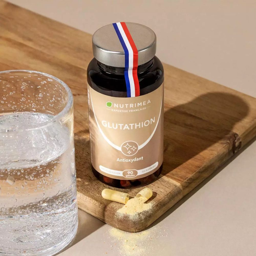 Flacon brun de gélules et verre d'eau. Inscription : GLUTATHION, 90 gélules. Sur une planche en bois.