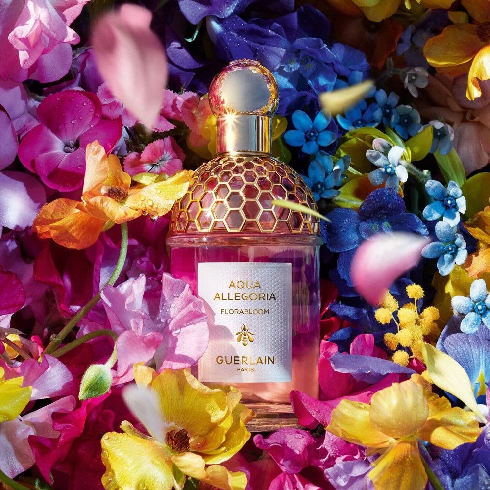Flacon de parfum avec bouchon doré, entouré de fleurs colorées. Inscription: Aqua Allegoria Florabloom, GUERLAIN.