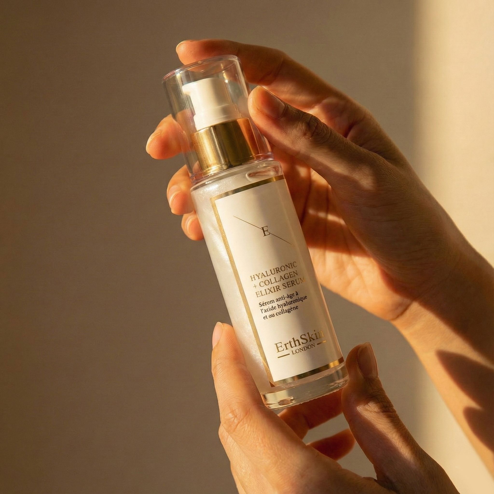 Handen houden een fles ErthSkin London Hyaluronzuur & Collageen Elixir Serum vast.
