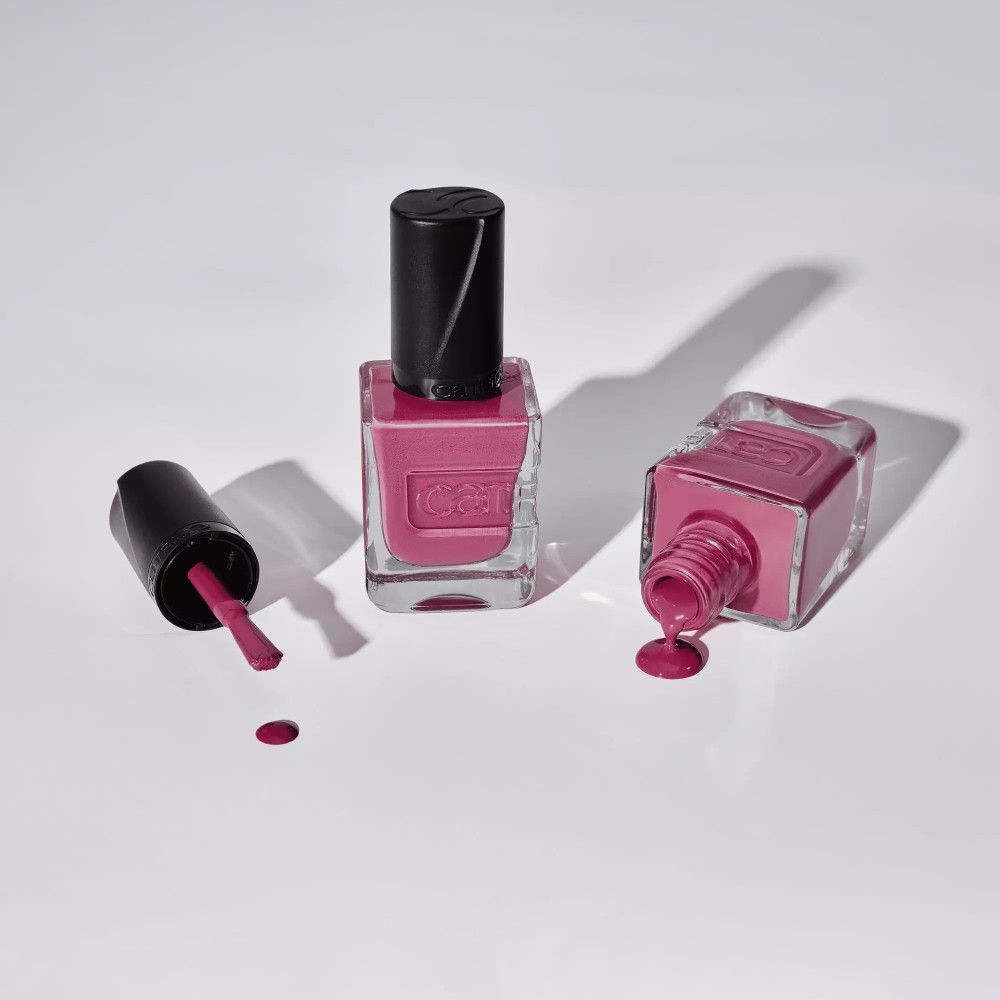 Trois flacons de vernis à ongles sur fond blanc. Un avec pinceau, deux renversés, vernis coulé. Marque Catrice.