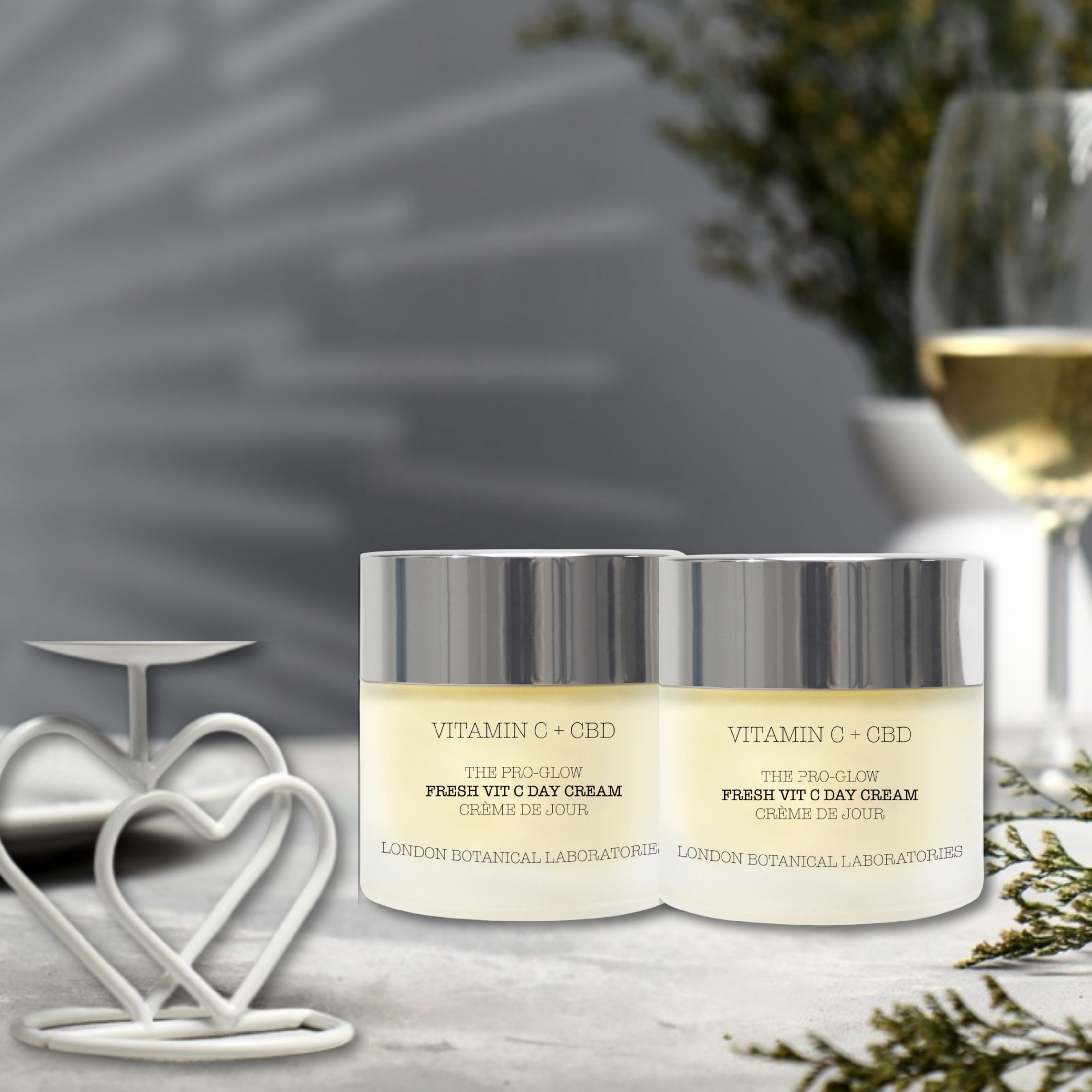 Twee crèmepotten met zilveren deksels. Opschrift: Vitamin C + CBD, The Pro-Glow Fresh Vitamin C Day Cream. Op lichte achtergrond.