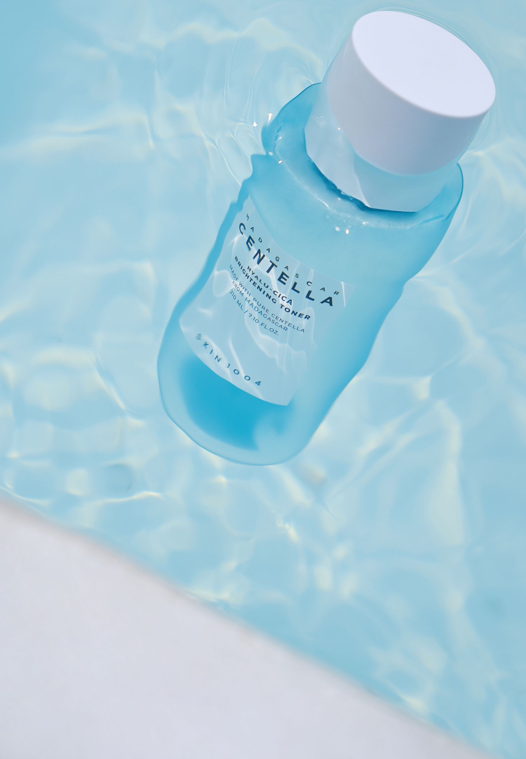 Lichtblauwe fles in water. Opschrift: MADAGASCAR CENTELLA HYALU-CICA BRIGHTENING TONER. SKIN1004.