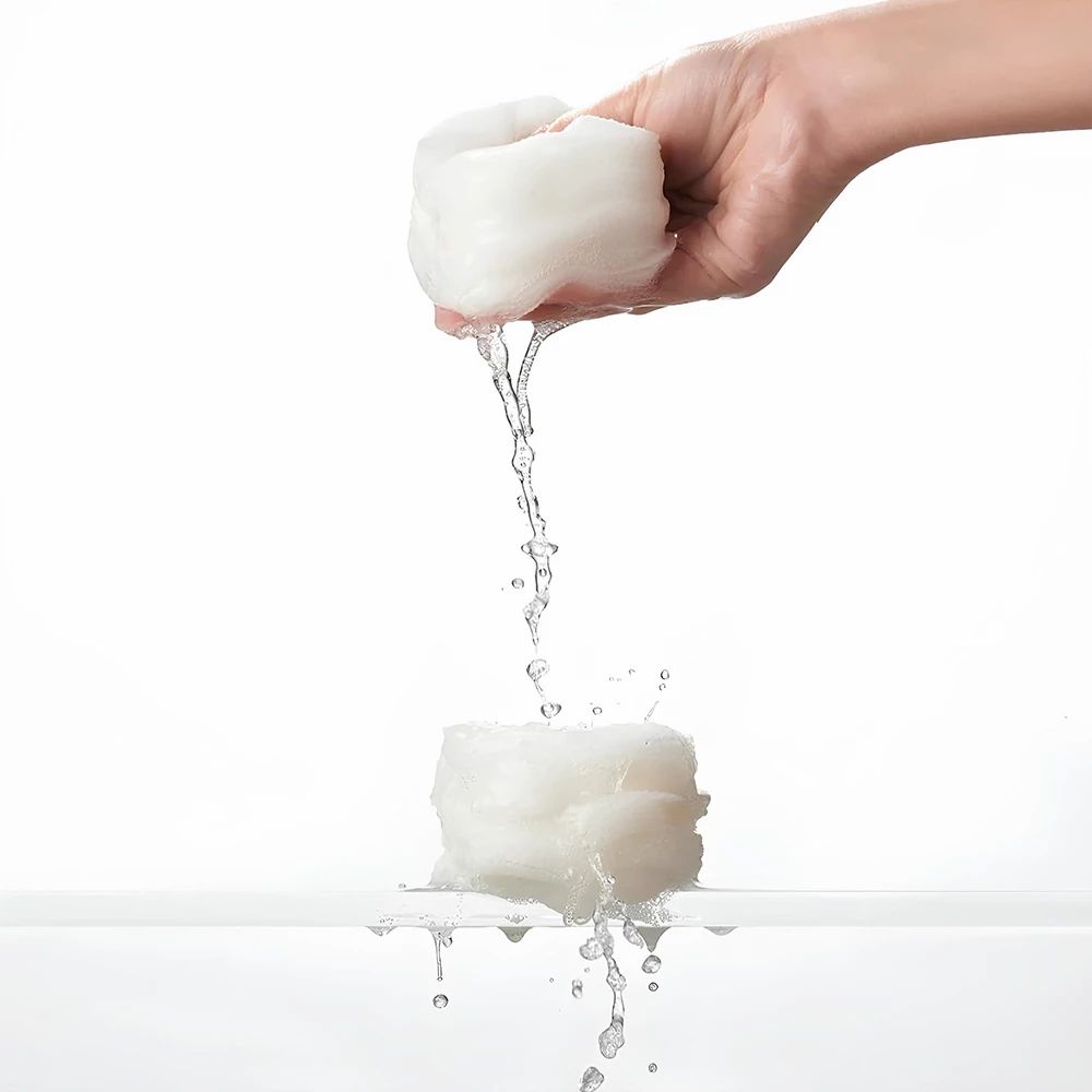 Hand houdt een pad vast, water stroomt eruit. Pad is wit en rond. Water spettert. Achtergrond wit.