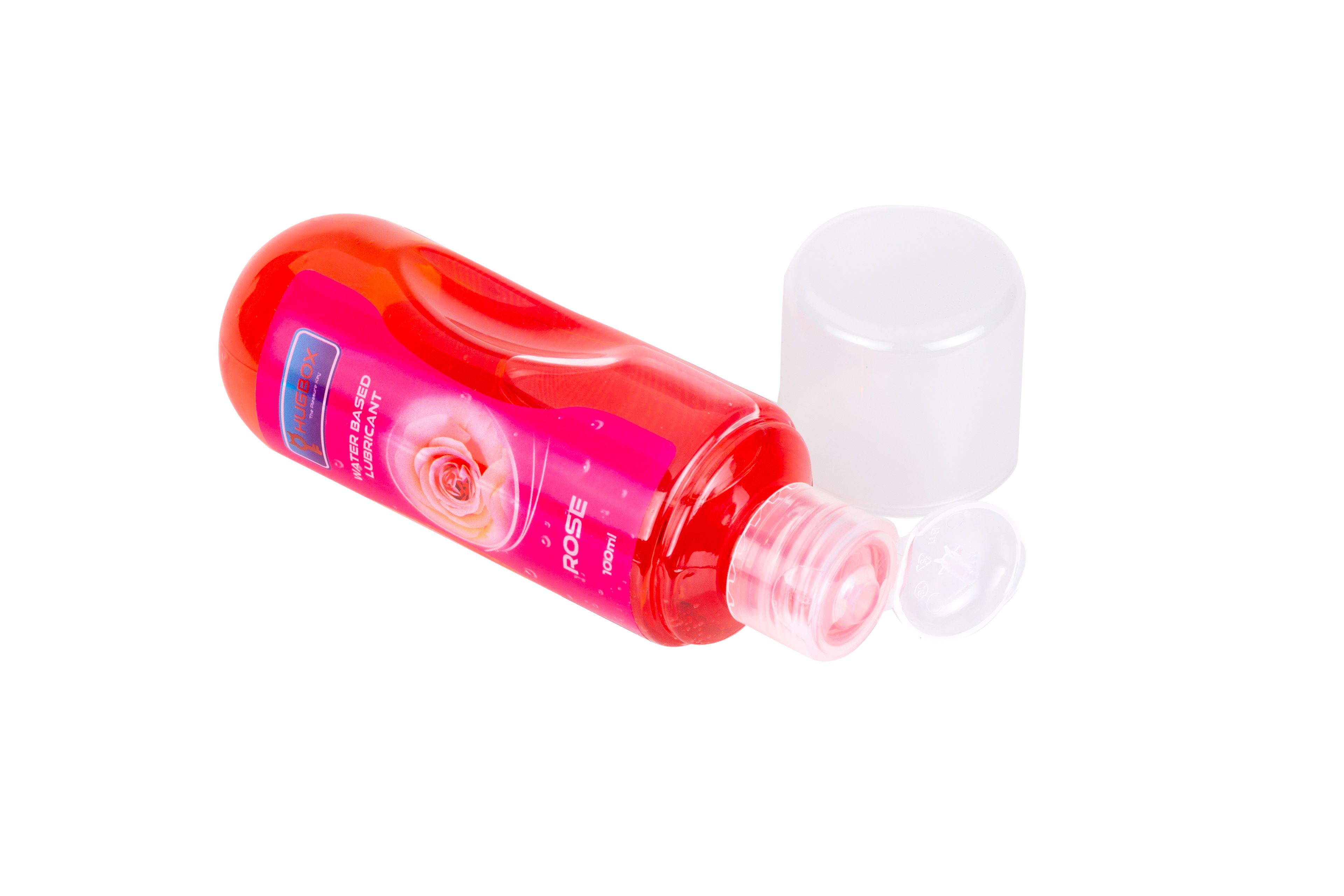 Flacon rouge, liquide rose, couché. Bouchon à côté. Étiquette avec texte et rose. Nom du produit non visible.