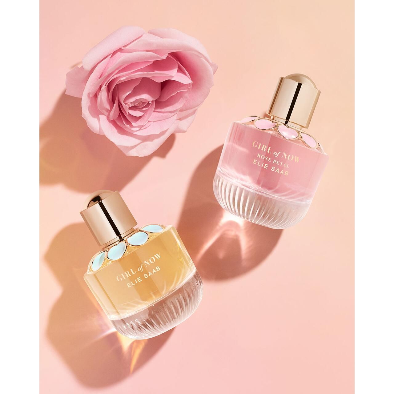 Twee parfumflesjes Girl of Now Rose Petal Elie Saab, gouden doppen, bloemdecoratie. Een roze roos ernaast.