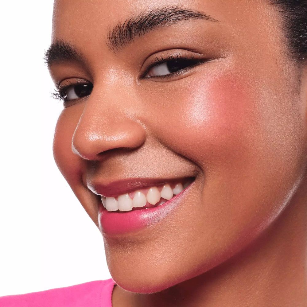 Close-up van een vrouw met roze wangen en lippen. Ze glimlacht. Huidtint en make-up zichtbaar.