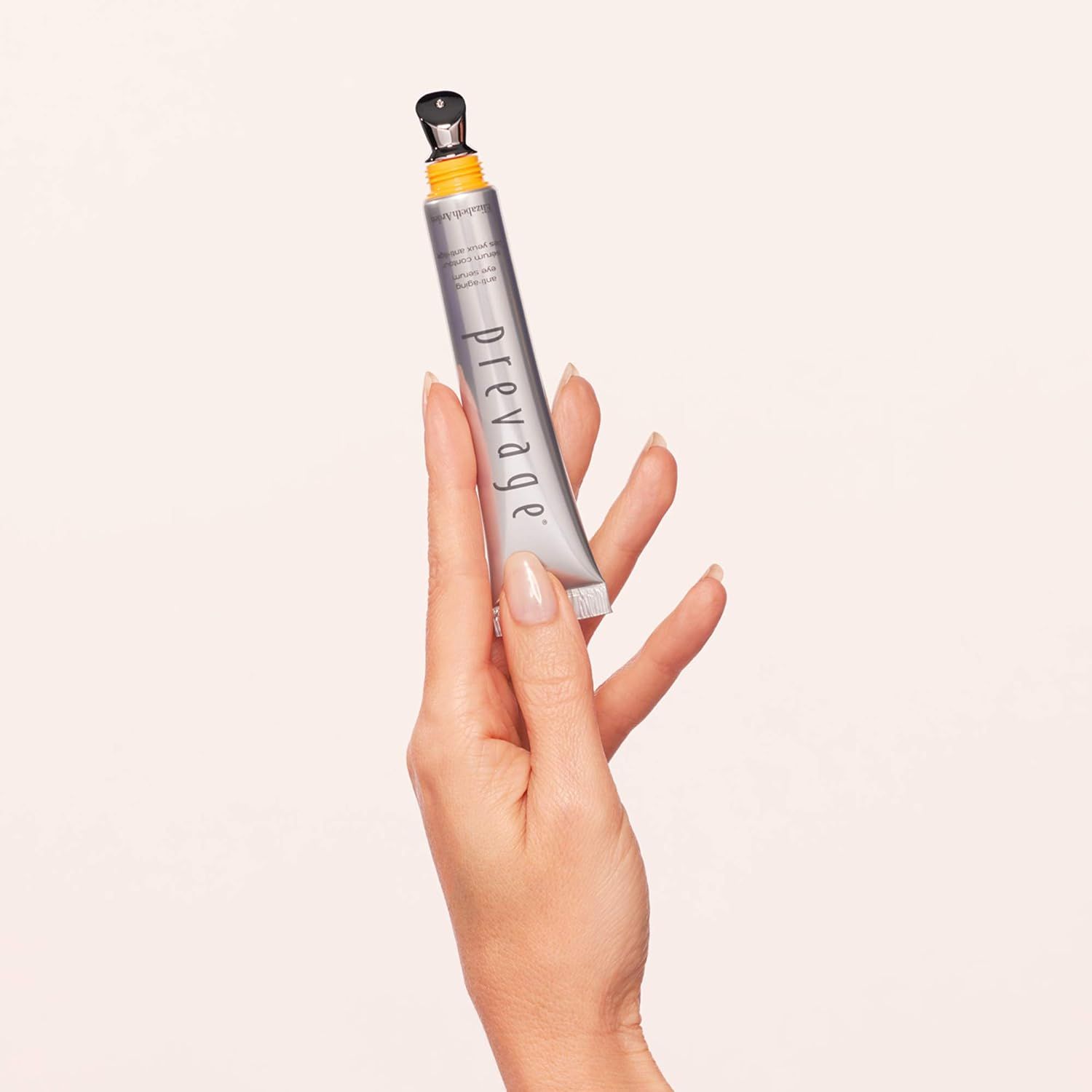 Zilveren tube met gele applicator en zwarte dop, vastgehouden in een hand.