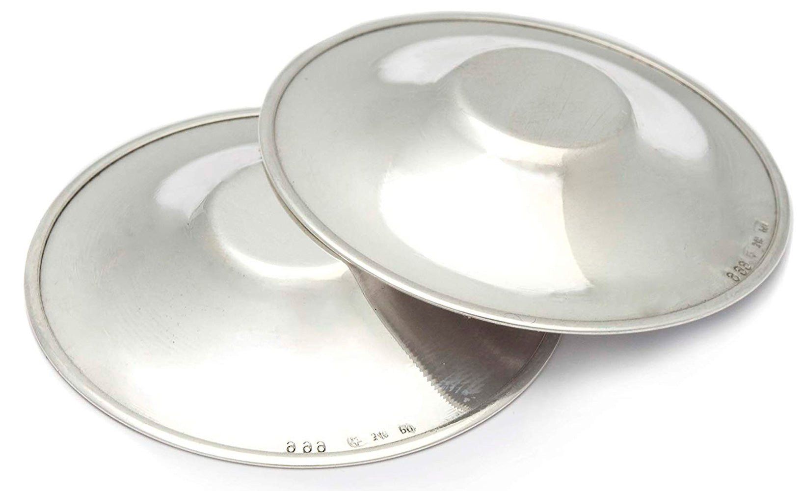 Deux protections d'allaitement argentées. Forme ronde avec partie centrale surélevée. Marquage visible.