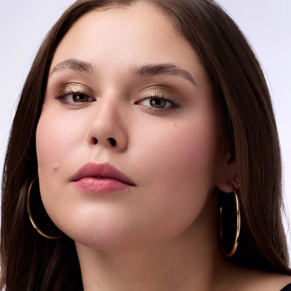 Portrait d'une femme avec fard à paupières doré. Elle porte des créoles dorées. Rouge à lèvres et fard à joues également visibles.