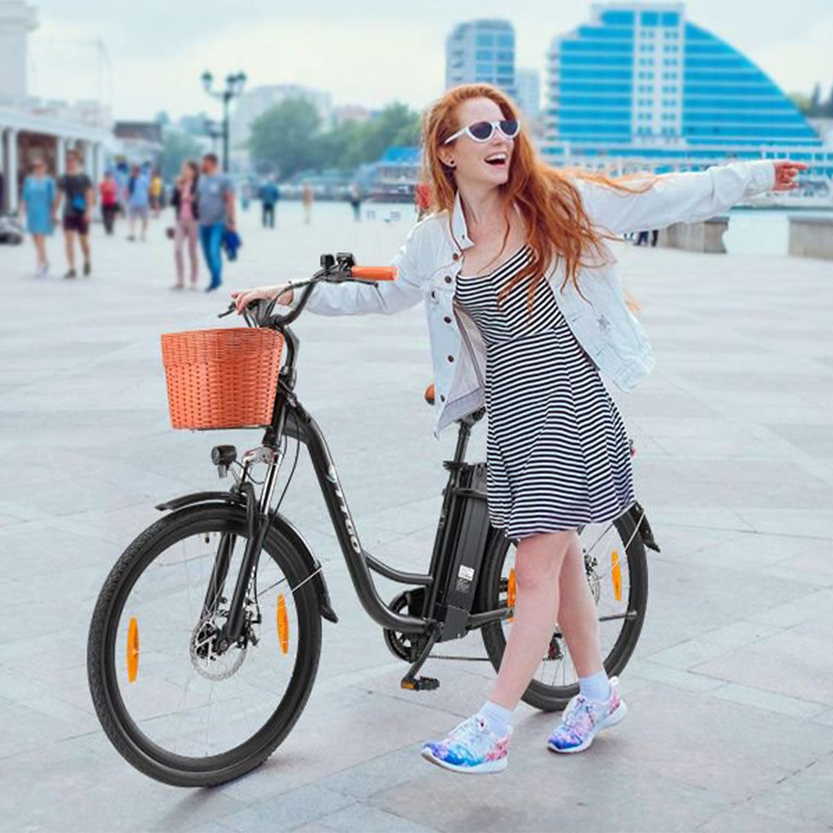 Femme avec vélo électrique noir. Panier, selle marron, poignées orange. Logo TTGO.