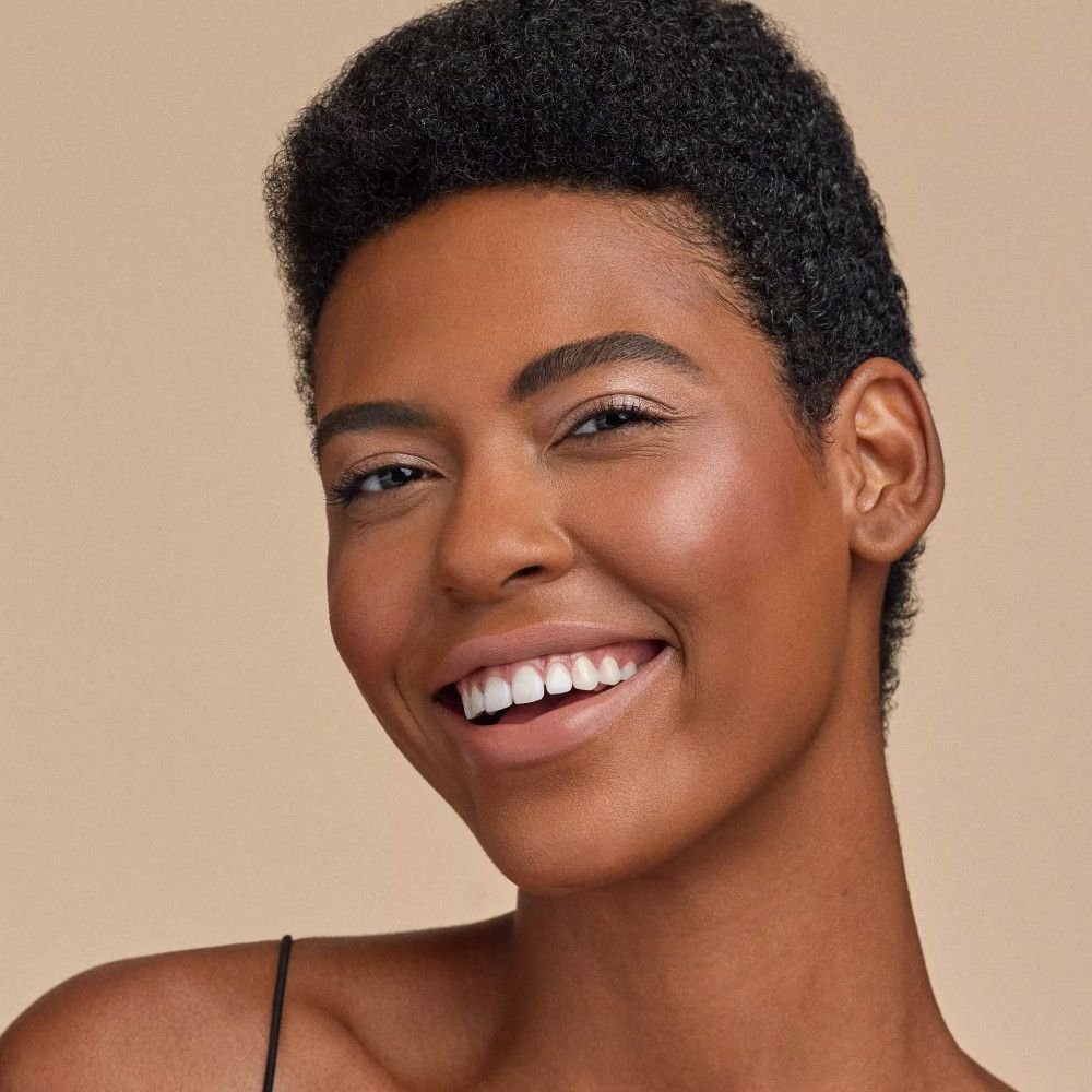 Portrait d'une femme à la peau foncée. Elle sourit. Peau avec effet brillant. Fond marron clair.