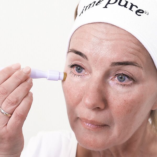 Een vrouw met een witte hoofdband gebruikt een huidroller bij haar oog.