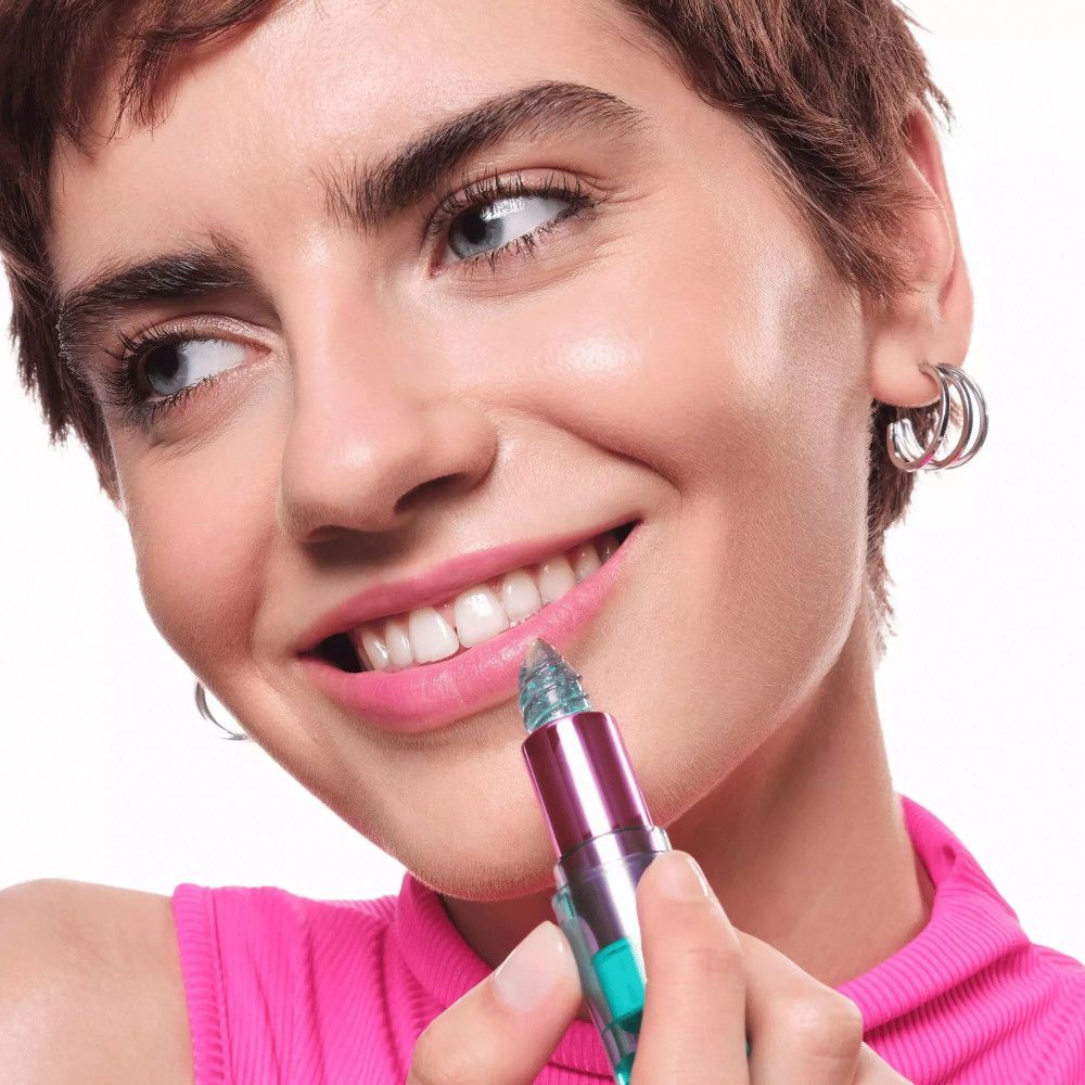 Une femme applique le rouge à lèvres Aqua Jelly. Elle sourit. Le rouge à lèvres est bleu et brillant.