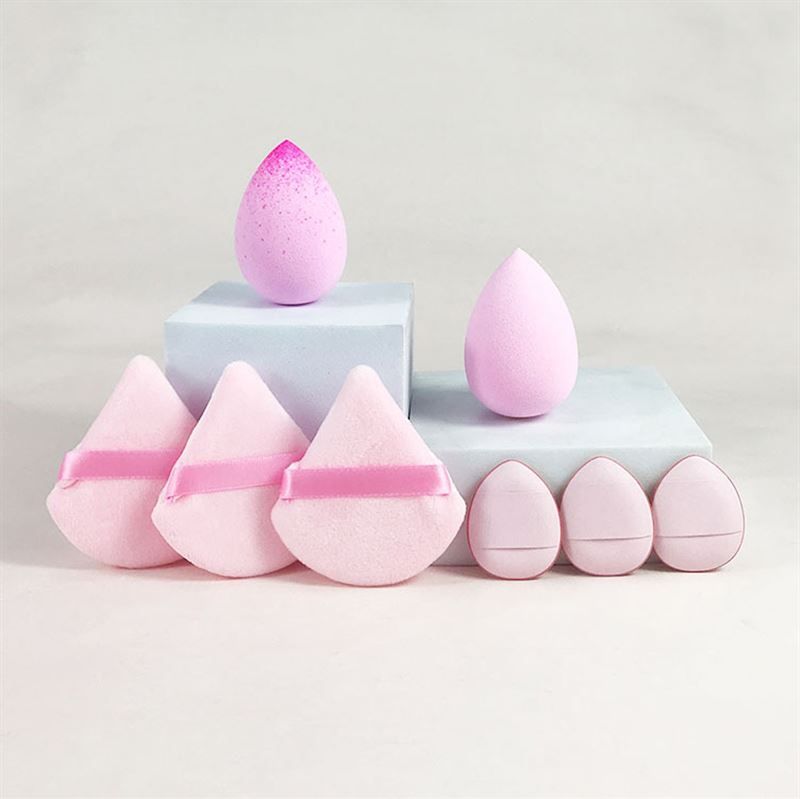 Plusieurs éponges de maquillage de formes et couleurs variées. Certaines en forme de goutte, d'autres triangulaires avec des rubans. Placées sur des socles.