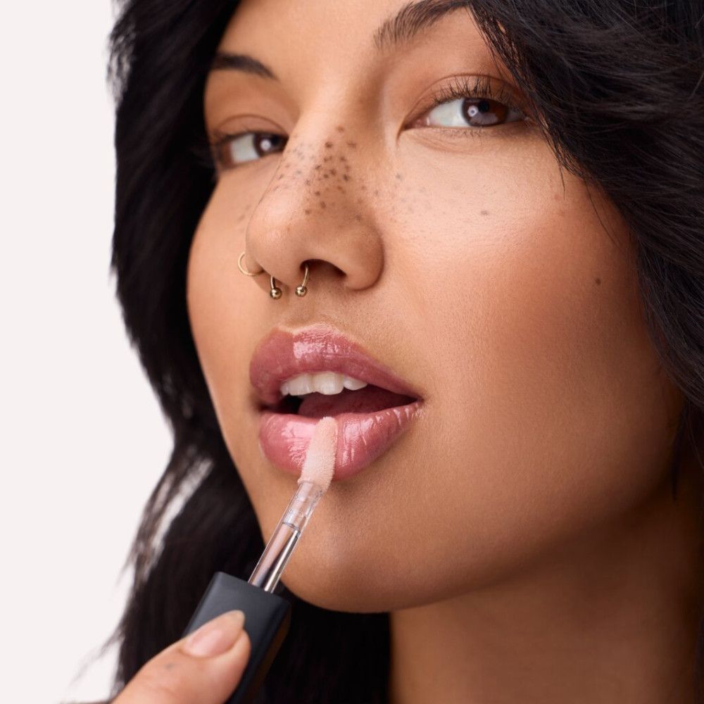 Personne avec applicateur de gloss. Lèvres avec gloss. Capuchon noir, applicateur transparent.