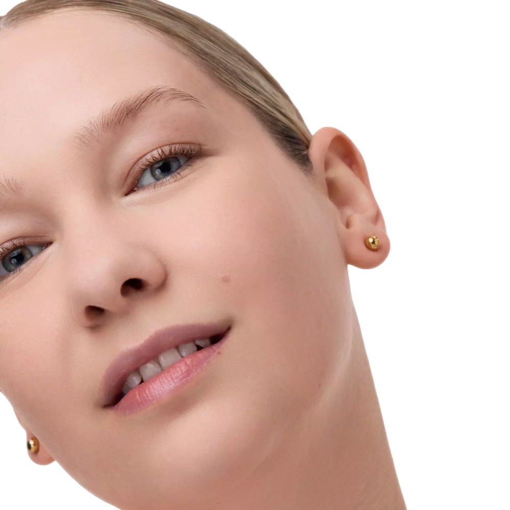 Portrait d'une femme. Elle porte des clous d'oreilles dorés. La peau est uniforme.