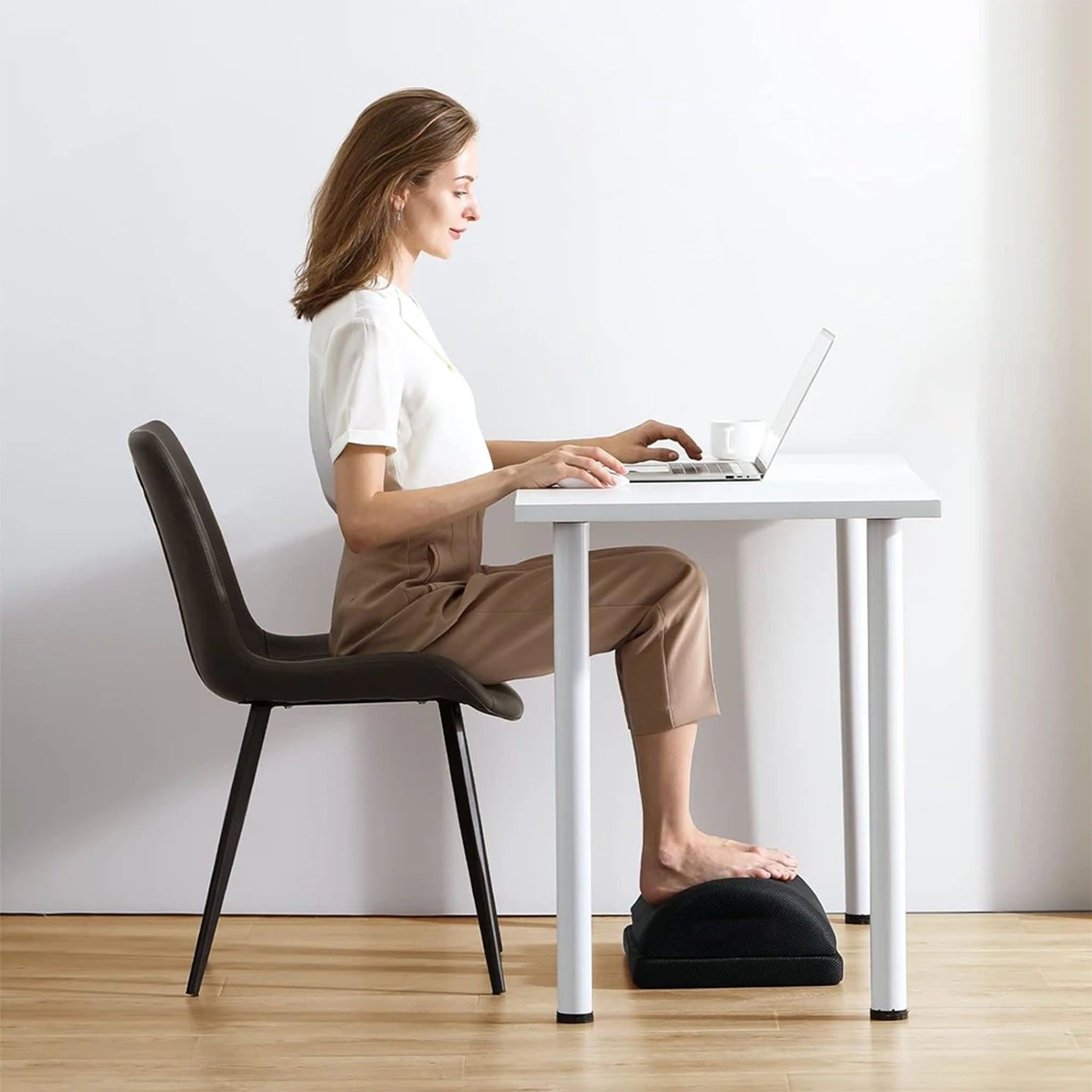 Vrouw zit aan een bureau, voeten op een ergonomische voetensteun.