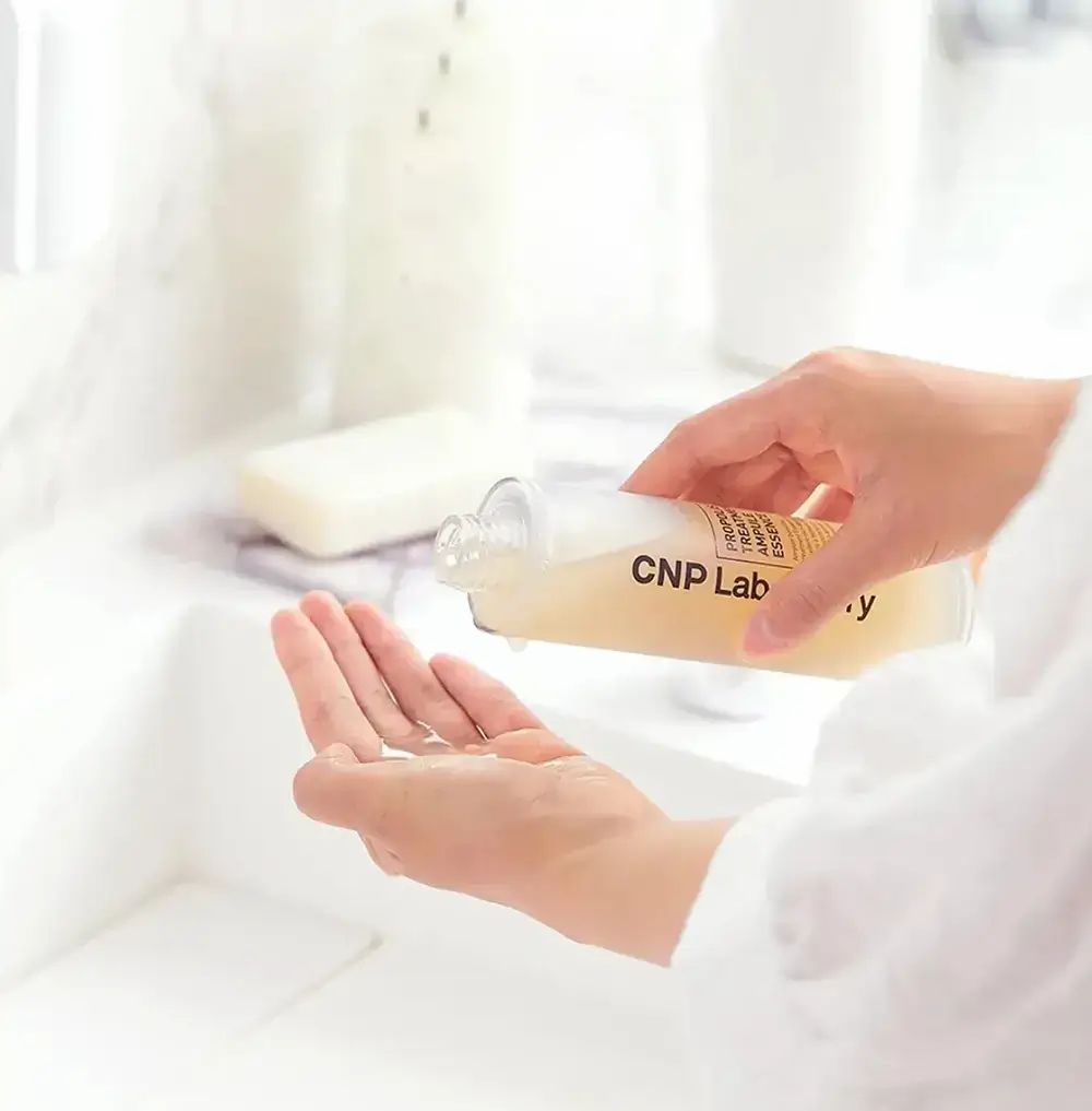 Persoon giet CNP Laboratory Propolis Treatment Ampoule in de hand. Fles met productlabel. Badkamerachtergrond.