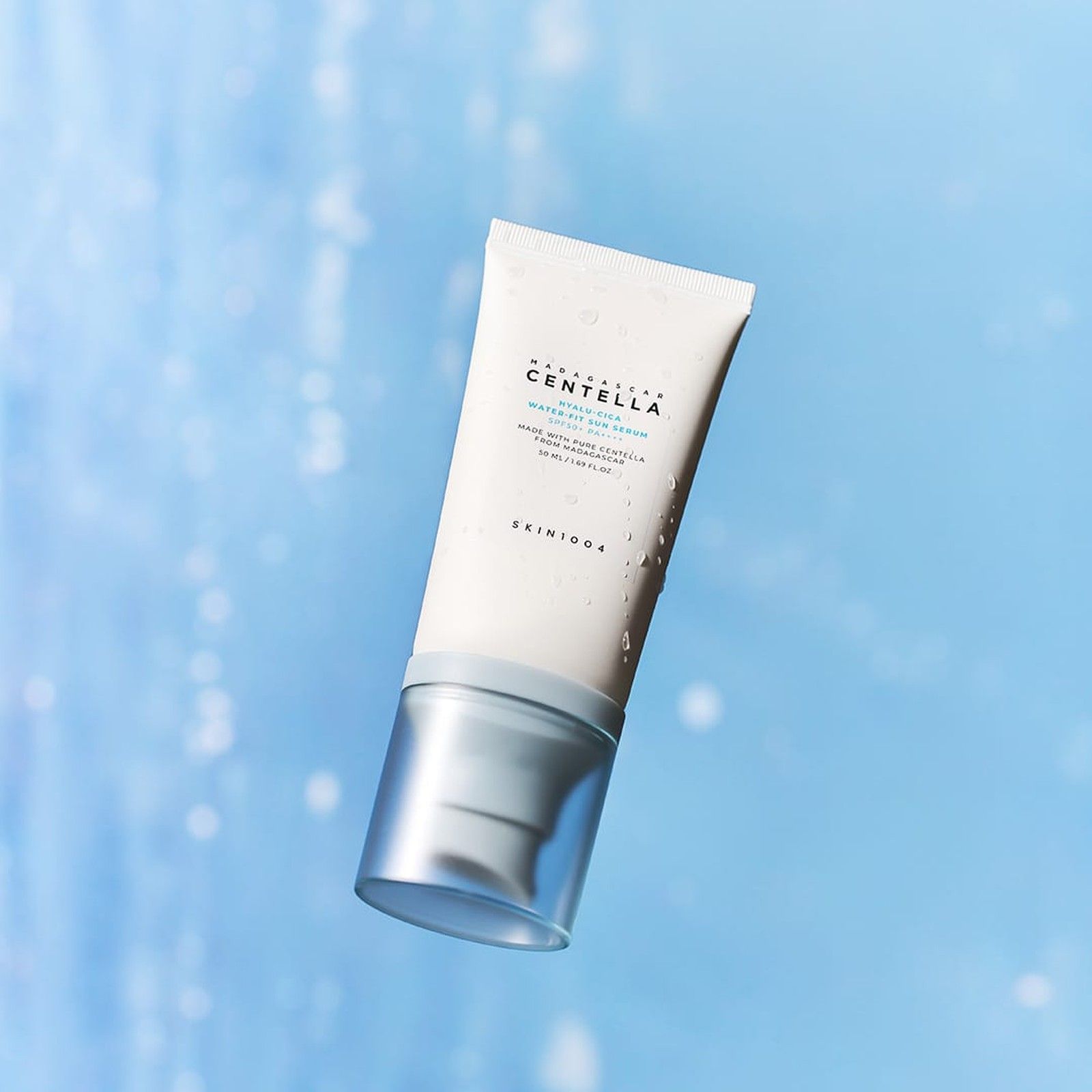 SKIN1004 Hyalu-Cica Water-Fit Sérum Solaire SPF 50+ PA++++ flotte sur un fond bleu flou.