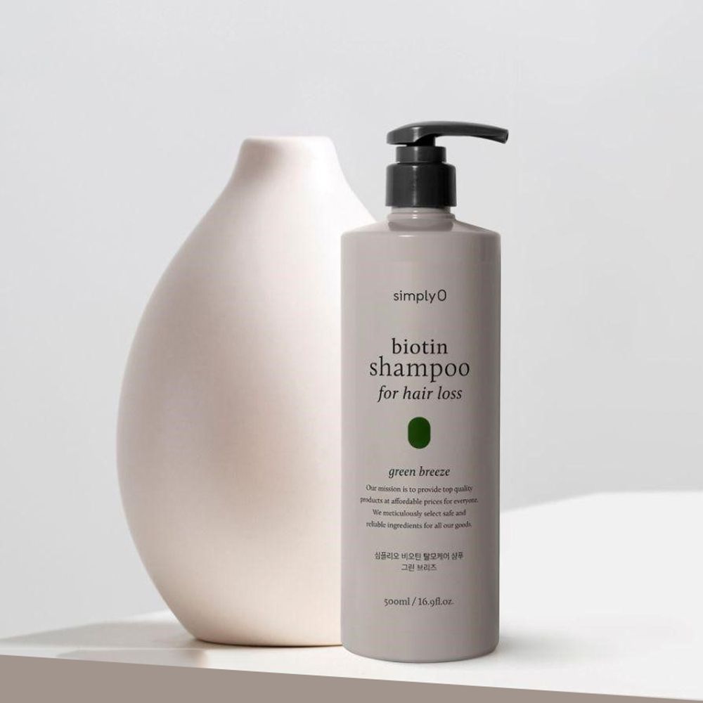 Grijze shampoo fles met zwarte pomp naast een witte vaas. Opschrift: Biotin Shampoo for hair loss.