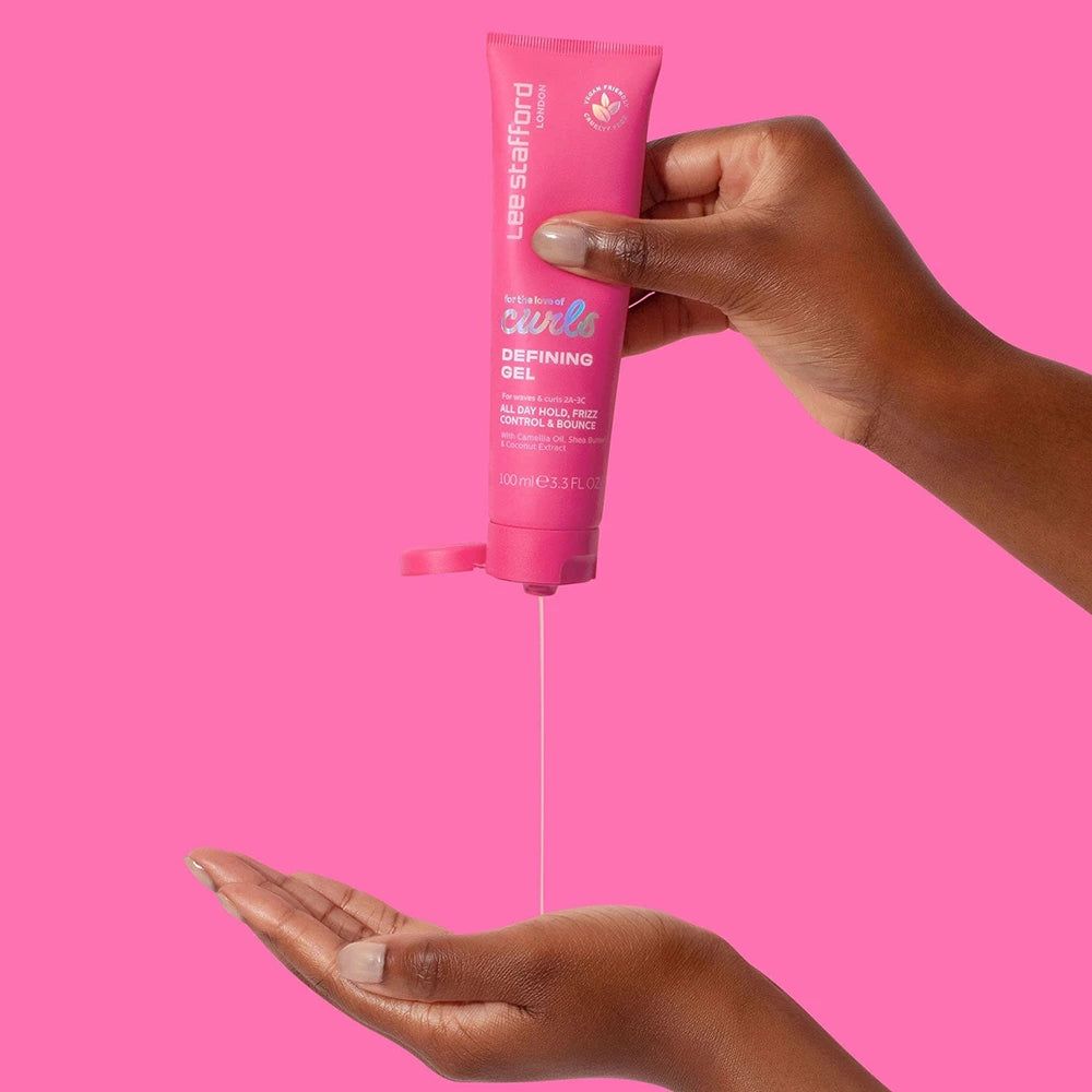 Main pressant Lee Stafford For The Love Of Curls Defining Gel d'un tube rose dans la paume.