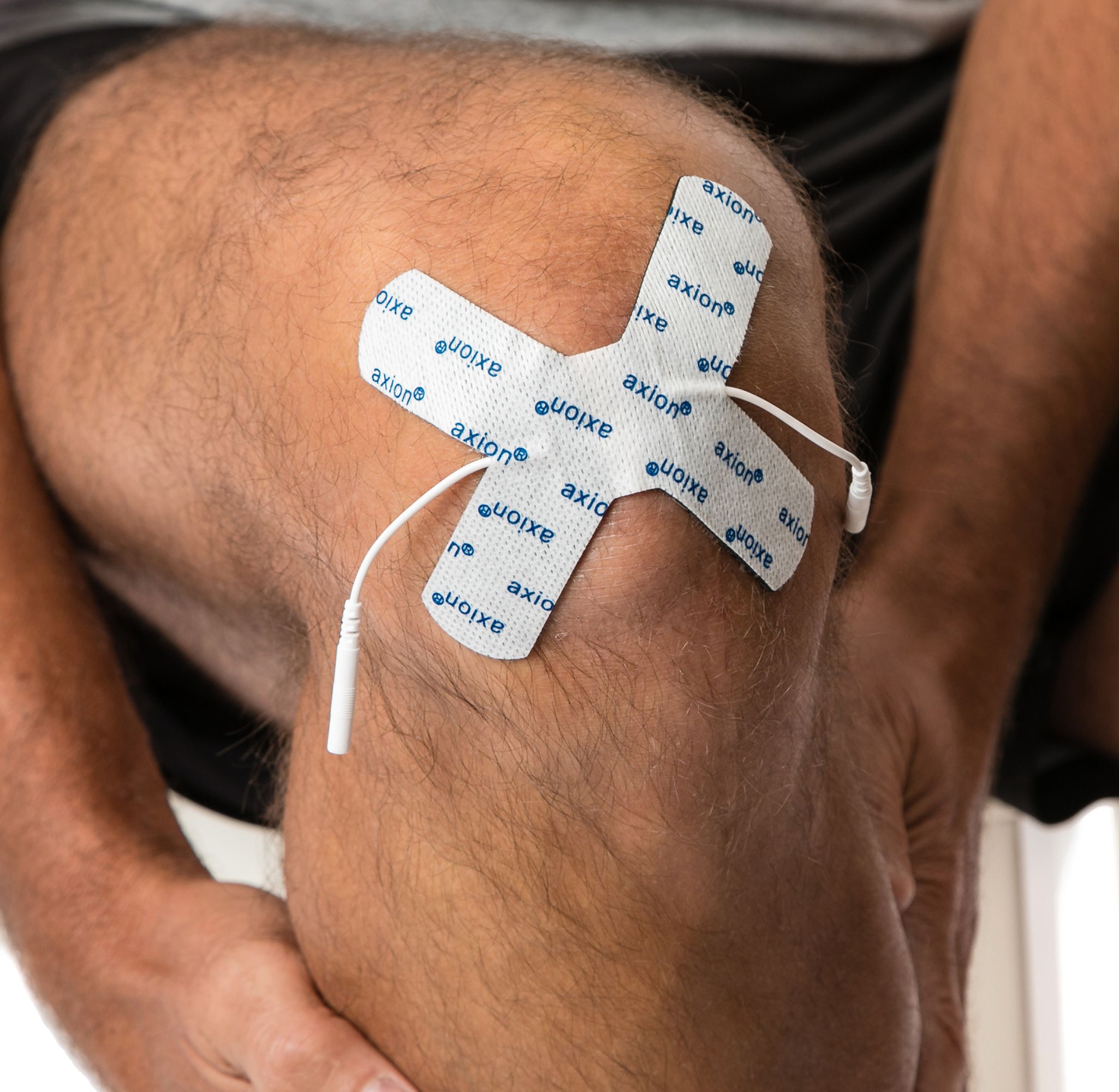 Elektrode in X-vorm op knie geplaatst. Wit met blauw axion®-logo. Met kabel en stekker.