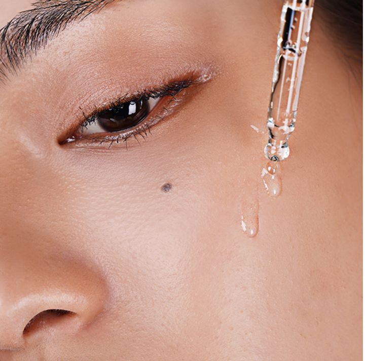 Gros plan sur un visage. Goutte de sérum d'une pipette sur la peau. Partie du visage avec œil, sourcil, grain de beauté.