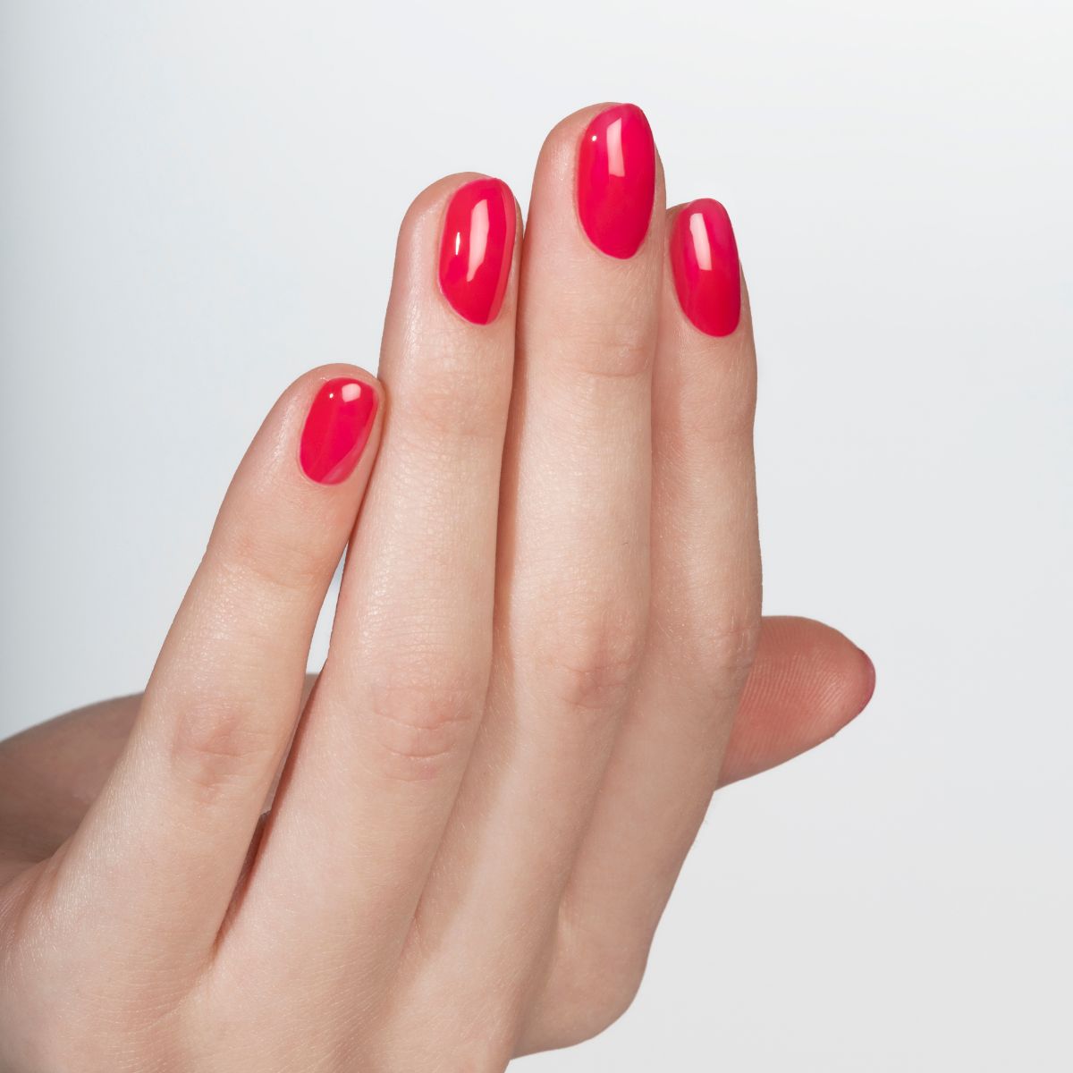 Main avec ongles vernis d'une couleur rouge vif. Les ongles sont courts et uniformément vernis.