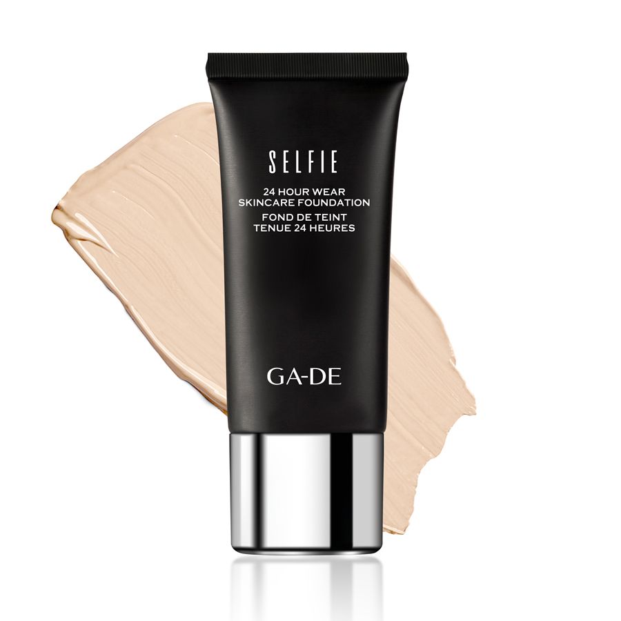 Tube noir avec logo GA-DE et inscription 'SELFIE 24 HOUR WEAR SKINCARE FOUNDATION'. À côté, un échantillon de fond de teint beige clair.