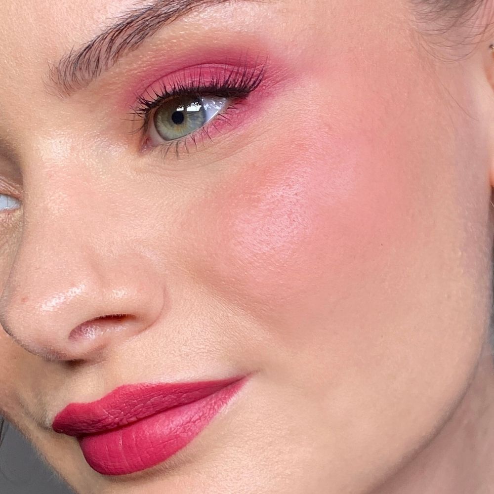 Gros plan d'un visage maquillé en rose. Fard à paupières, blush et rouge à lèvres roses. Œil vert.