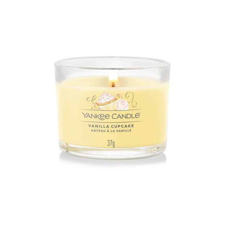 Bougie en verre avec cire jaune. Inscription: Yankee Candle Vanilla Cupcake, 37g. Flamme allumée.