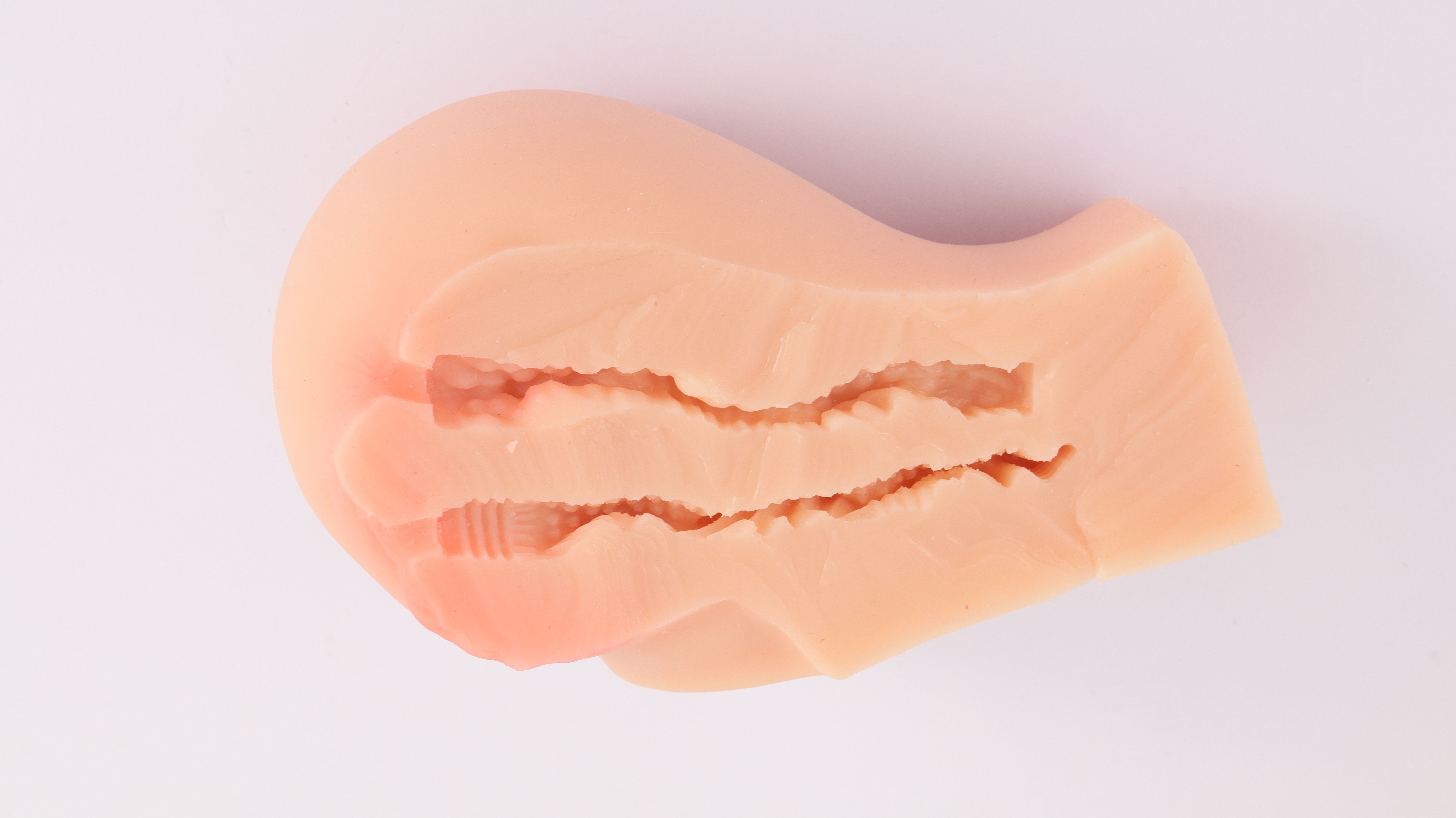 Beige, anatomisch gevormd product met interne groeven. Op witte achtergrond.