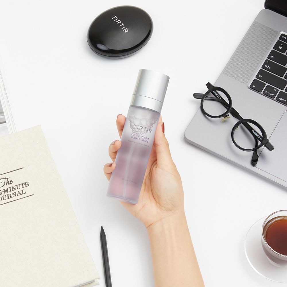 Hand houdt TIRTIR Collagen Core Glow Essence vast naast een notitieboek en een bril.